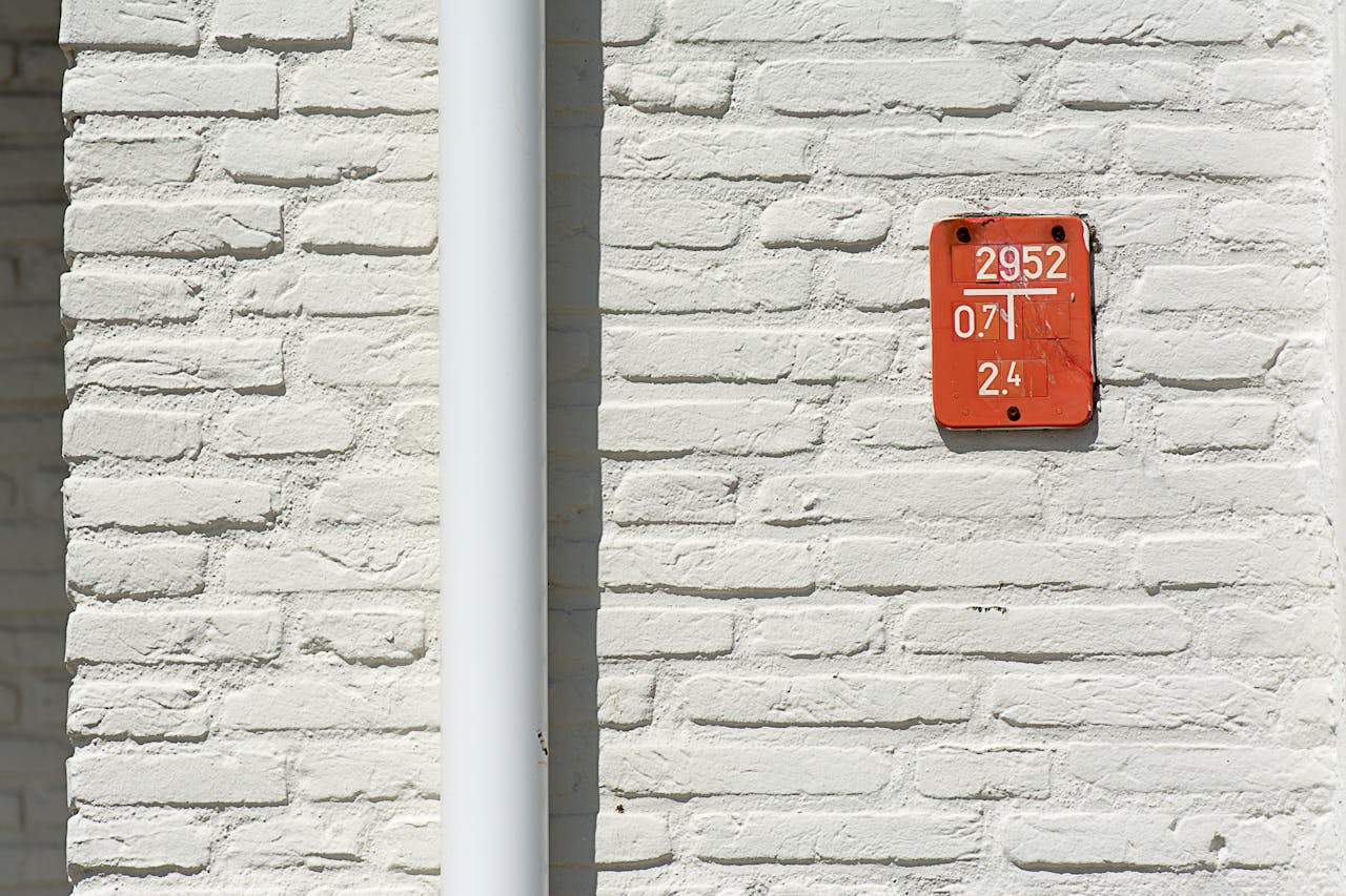 services-02 Close-up of a white brick wall featuring a red numbered sign with a white gutter pipe.