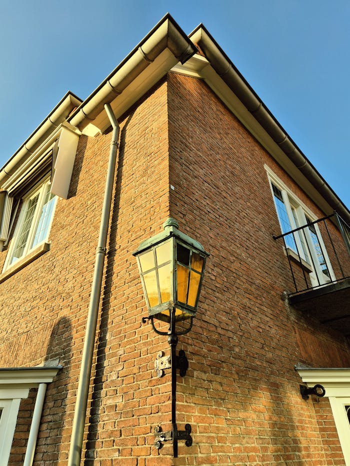 hero-img-02 Corner view of a brick house with a vintage lantern under clear skies.